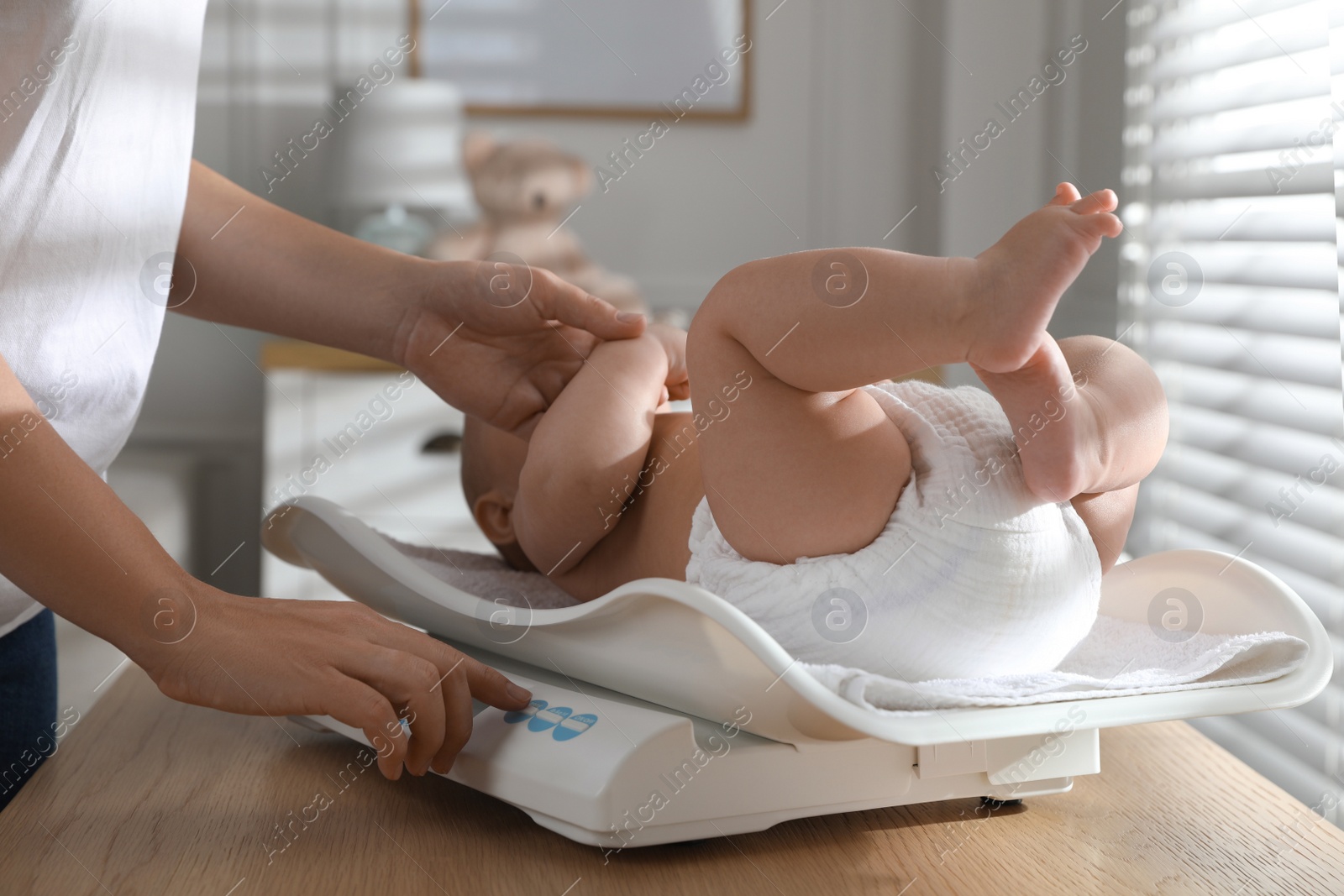 Photo of Young woman weighting her cute baby at home, closeup. Health care