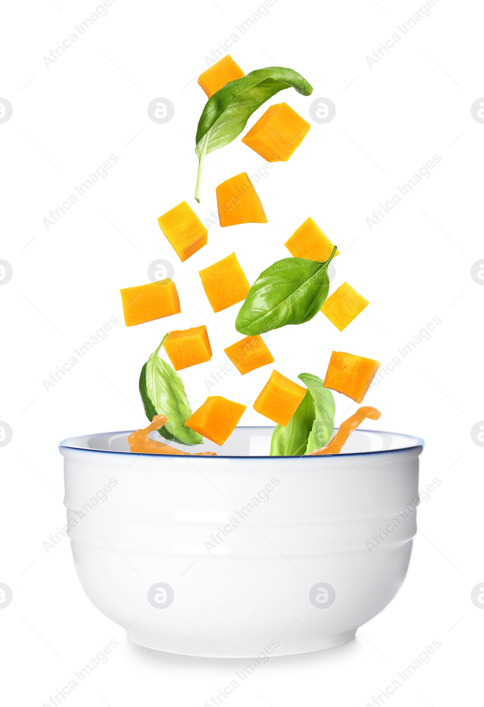 Image of Ingredients falling into bowl of homemade pumpkin soup on white background 