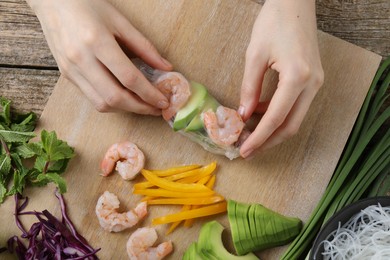 Photo of Woman wrapping spring roll at wooden table with products, top view