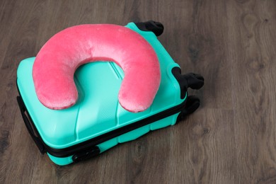 Photo of Pink travel pillow and turquoise suitcase on floor