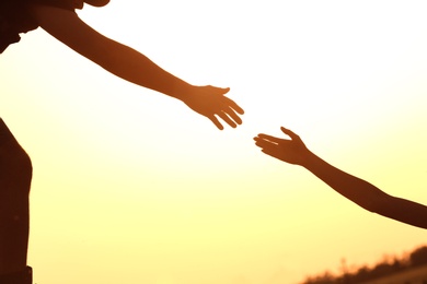 Silhouettes of man and woman helping each other to climb on hill against sunset, closeup