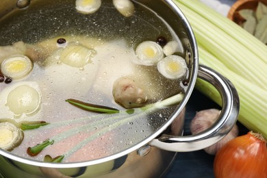 Pot with tasty bouillon and different ingredients on table, closeup