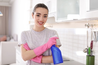 Photo of Young woman with bottle of detergent in kitchen