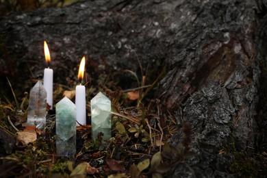 Photo of Different crystals and burning candles near tree outdoors, space for text
