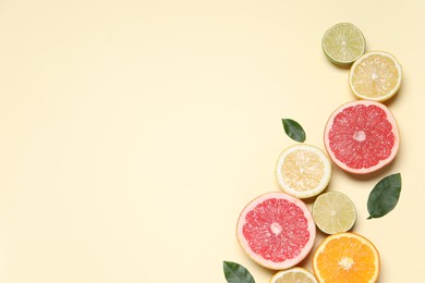 Photo of Different cut citrus fruits and leaves on beige table, flat lay. Space for text