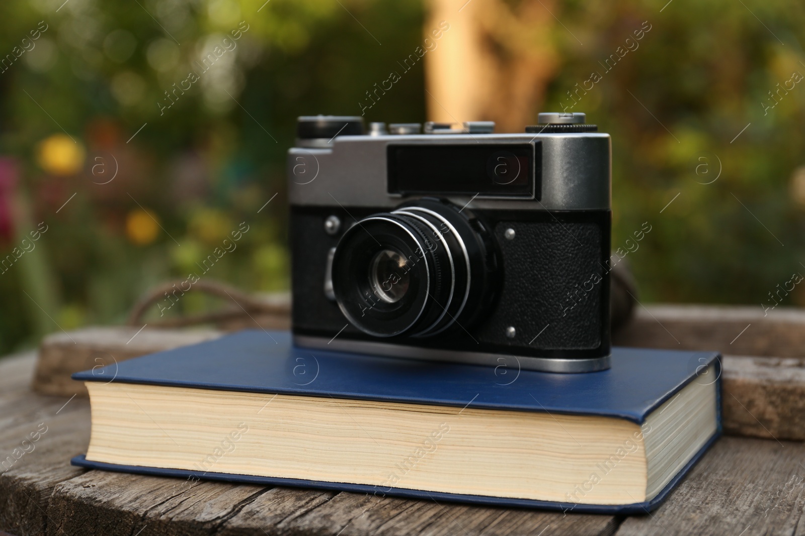 Photo of Hardcover book and vintage camera on wooden table outdoors