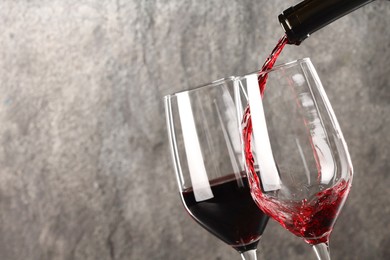 Photo of Pouring red wine into glass against grey background, closeup. Space for text