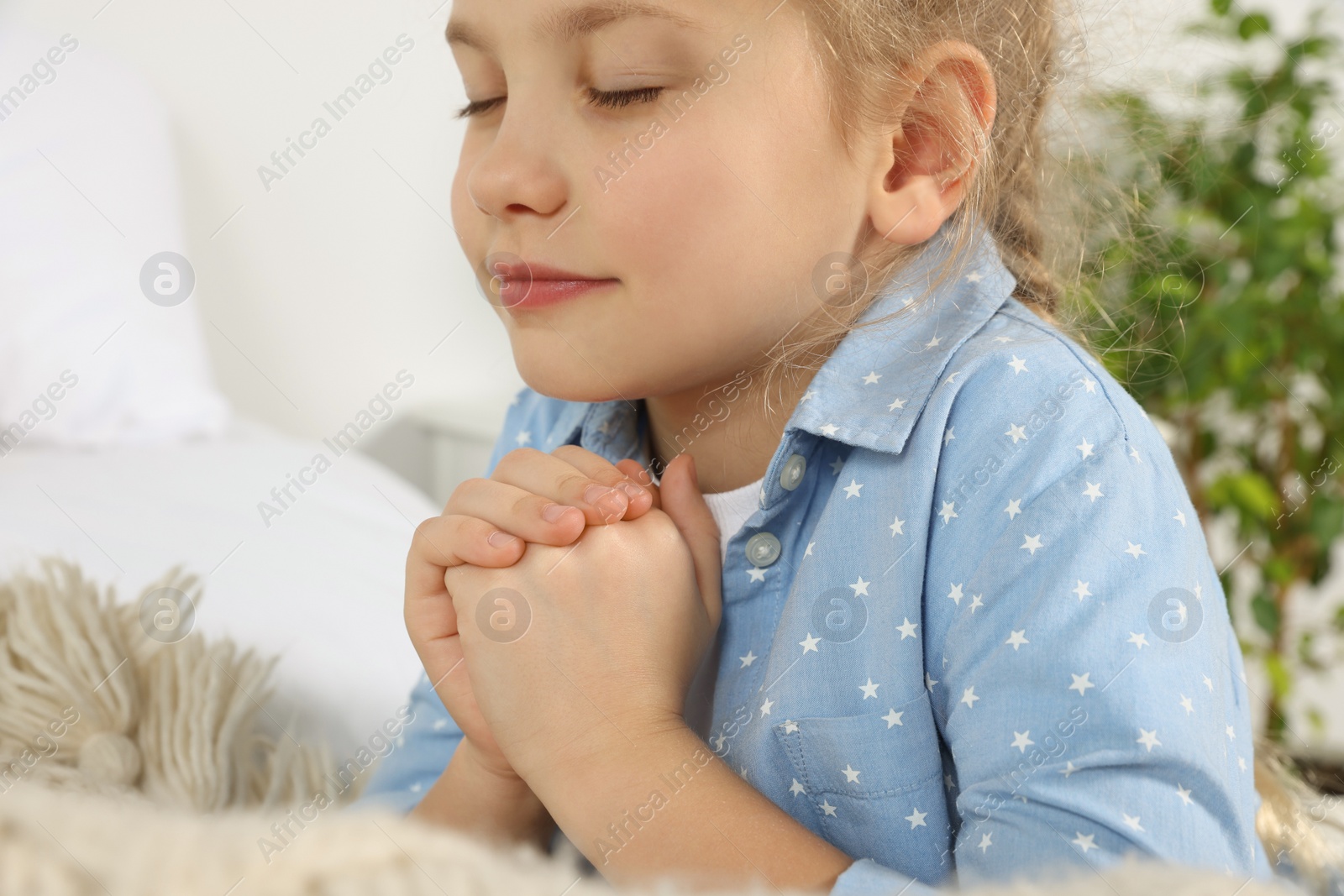 Photo of Girl with clasped hands praying near bed, closeup