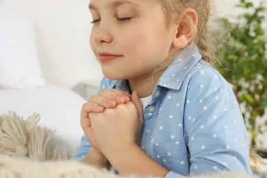Photo of Girl with clasped hands praying near bed, closeup