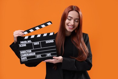 Happy actress with clapperboard on orange background. Film industry