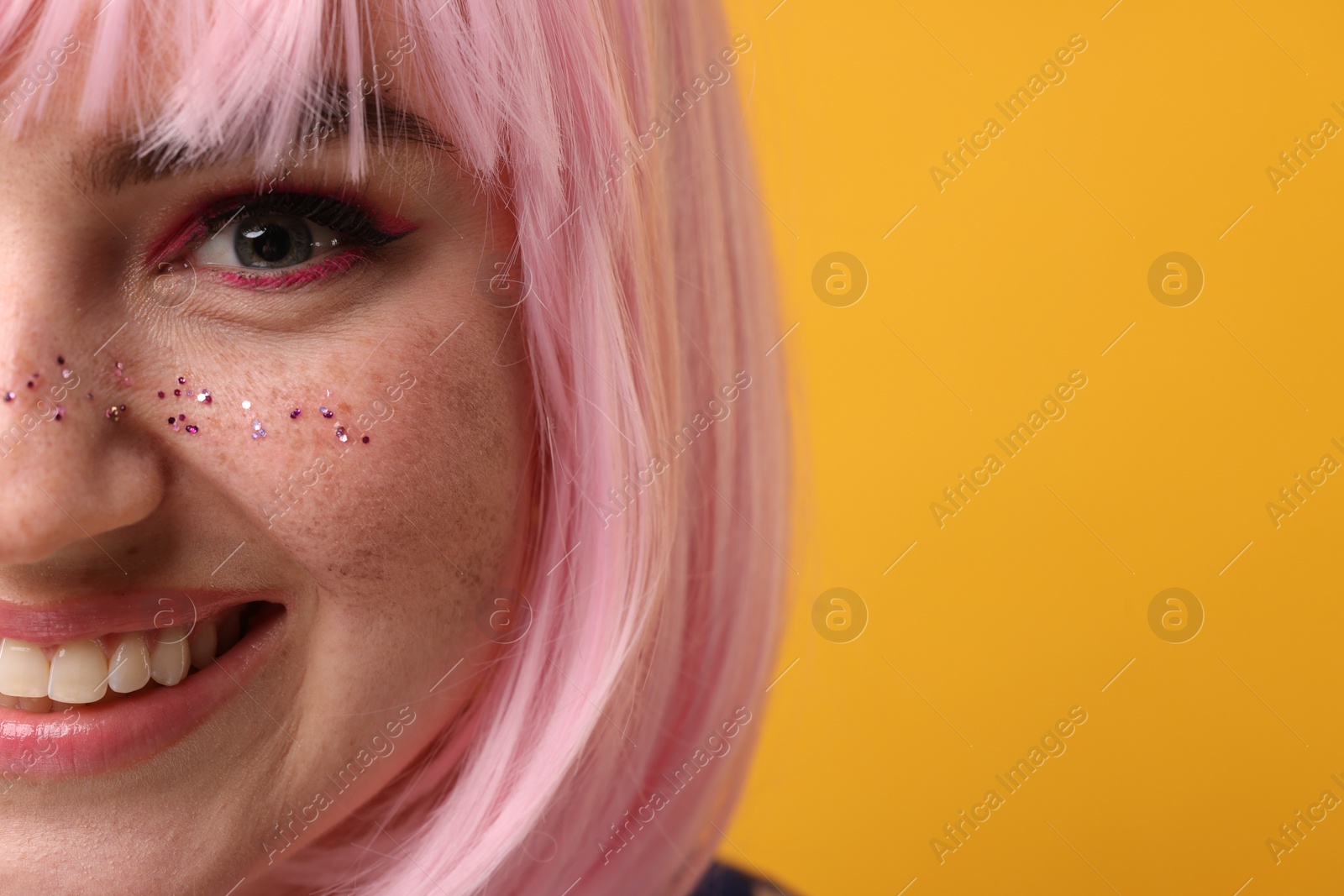 Photo of Smiling woman with bright makeup and glitter freckles on yellow background, closeup. Space for text