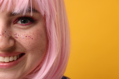 Smiling woman with bright makeup and glitter freckles on yellow background, closeup. Space for text