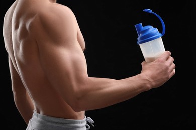 Young man with muscular body holding shaker of protein on black background, closeup