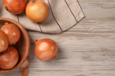 Many ripe onions on wooden table, flat lay. Space for text