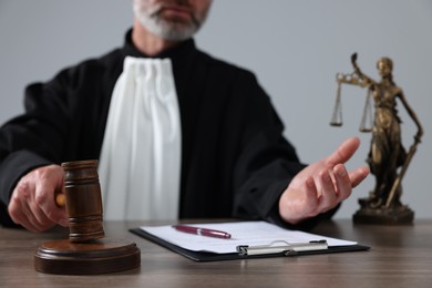 Judge with gavel and papers sitting at wooden table against light grey background, closeup