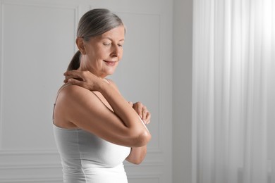 Happy woman applying body cream on elbow indoors. Space for text