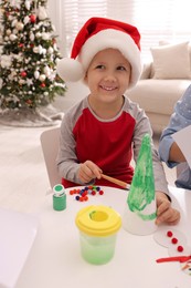 Cute little child making Christmas craft at table in decorated room