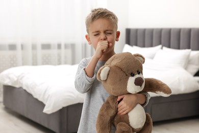 Photo of Sick boy with teddy bear coughing at home