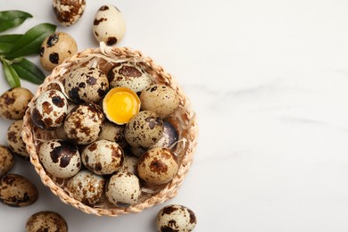 Photo of Wicker bowl with whole and cracked quail eggs on white marble table, flat lay. Space for text