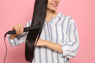 Photo of Happy woman using hair iron on pink background, closeup