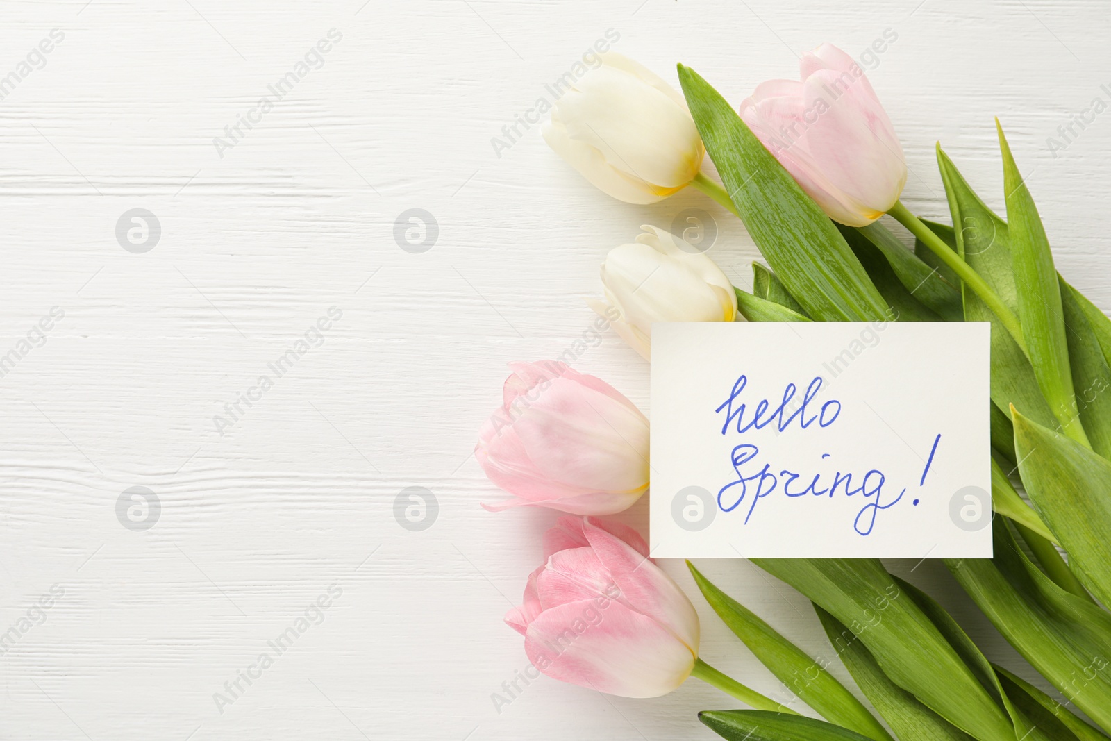 Photo of Card with words HELLO SPRING and tulips on white wooden table, flat lay. Space for text