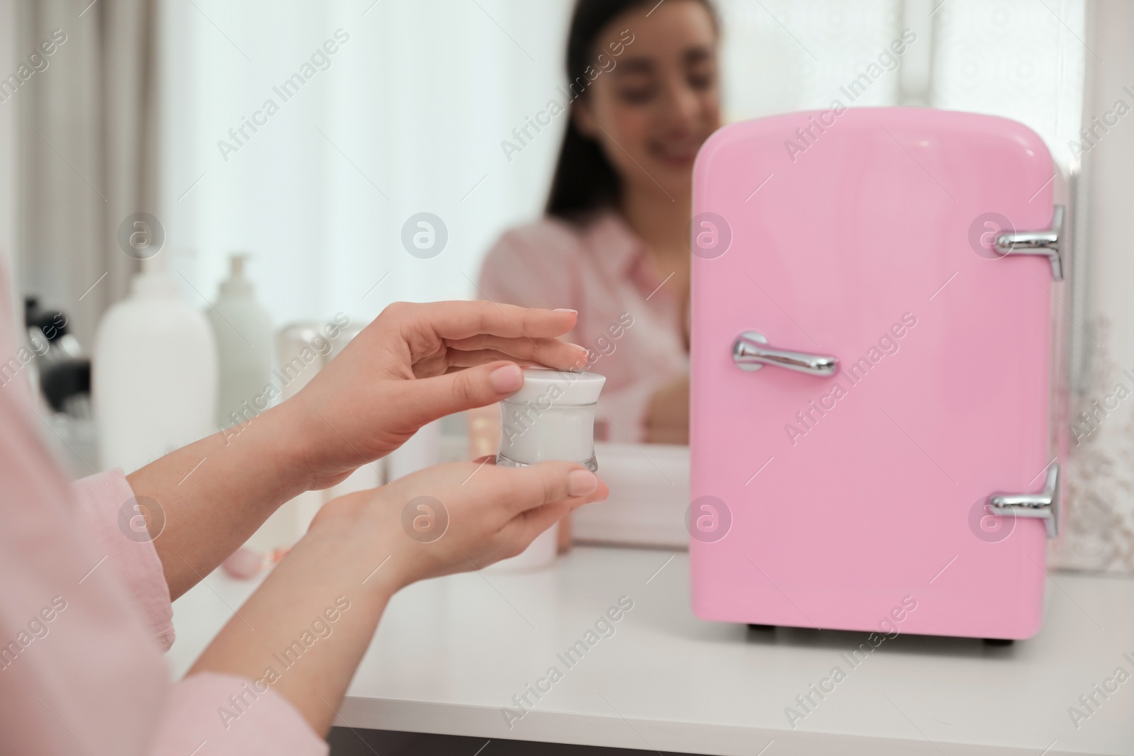 Photo of Woman getting ready at dressing table with cosmetic refrigerator indoors, closeup