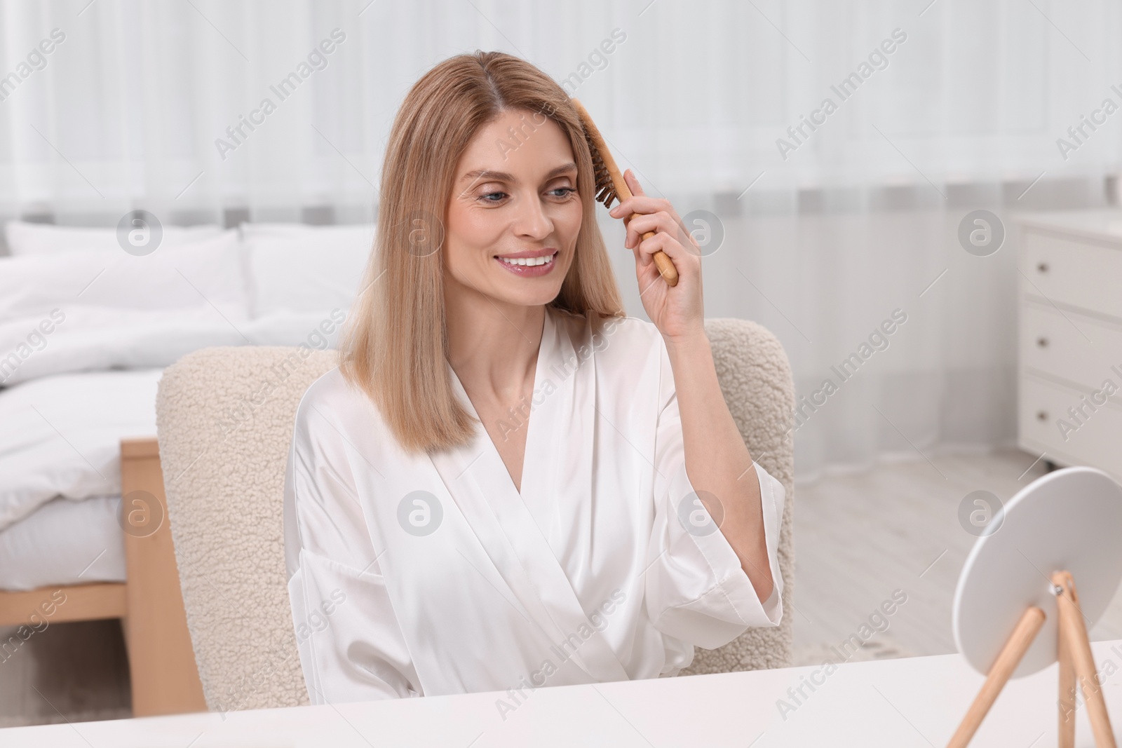 Photo of Beautiful woman brushing her hair at vanity in bedroom