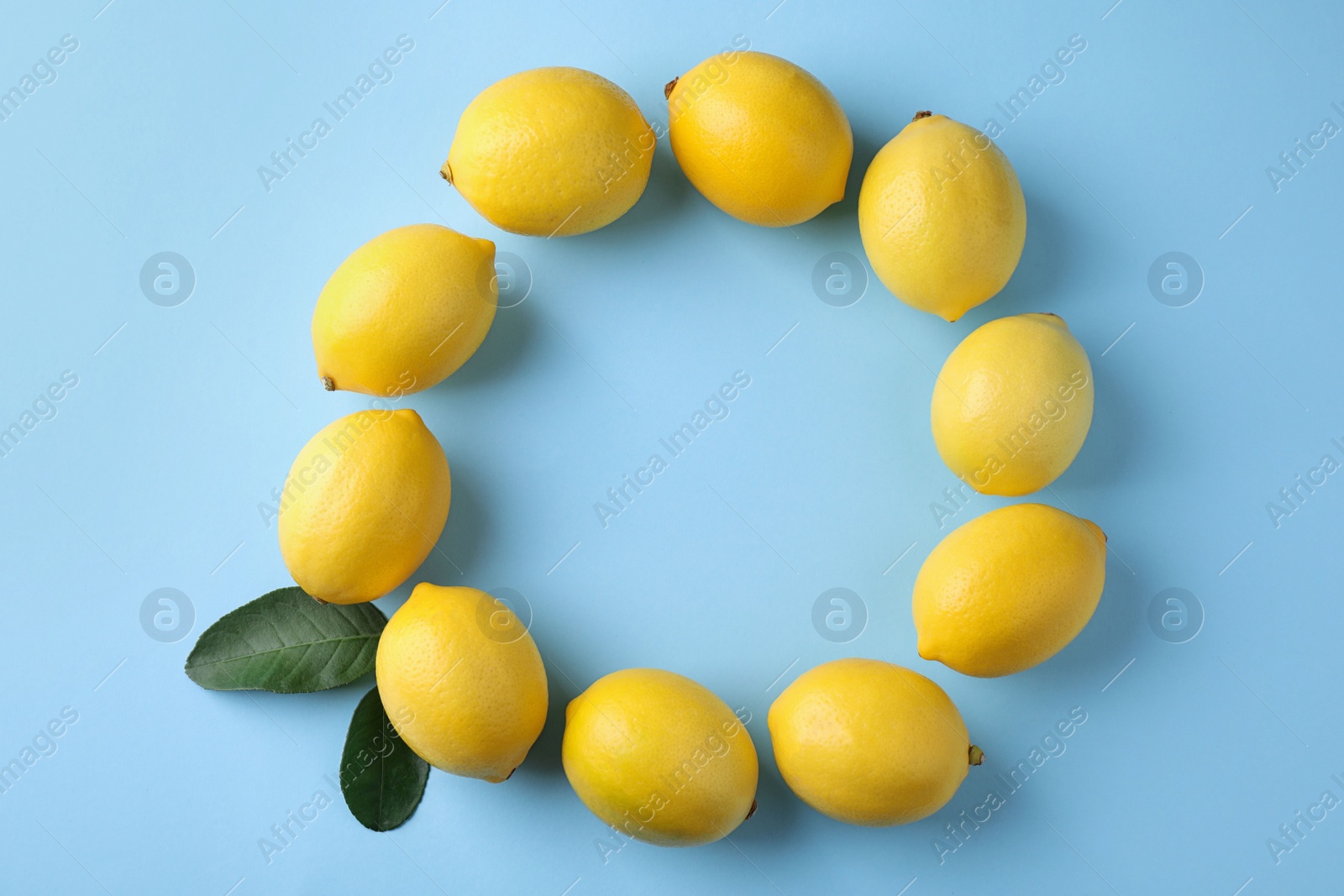 Photo of Frame made with ripe lemons and leaves on light blue background, top view. Space for text