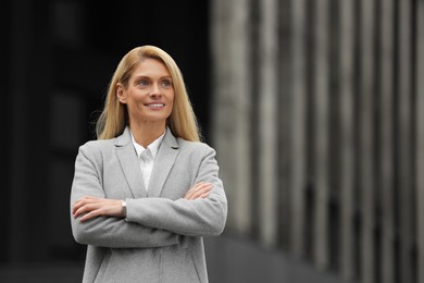 Photo of Smiling woman with crossed arms outdoors, space for text. Lawyer, businesswoman, accountant or manager