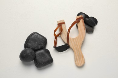 Photo of Wooden slingshot with stones on white background, flat lay