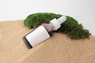 Photo of Bottle of serum and moss on sand against white background, closeup. Cosmetic product