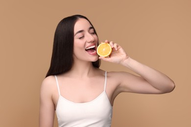 Beautiful young woman with piece of orange on beige background