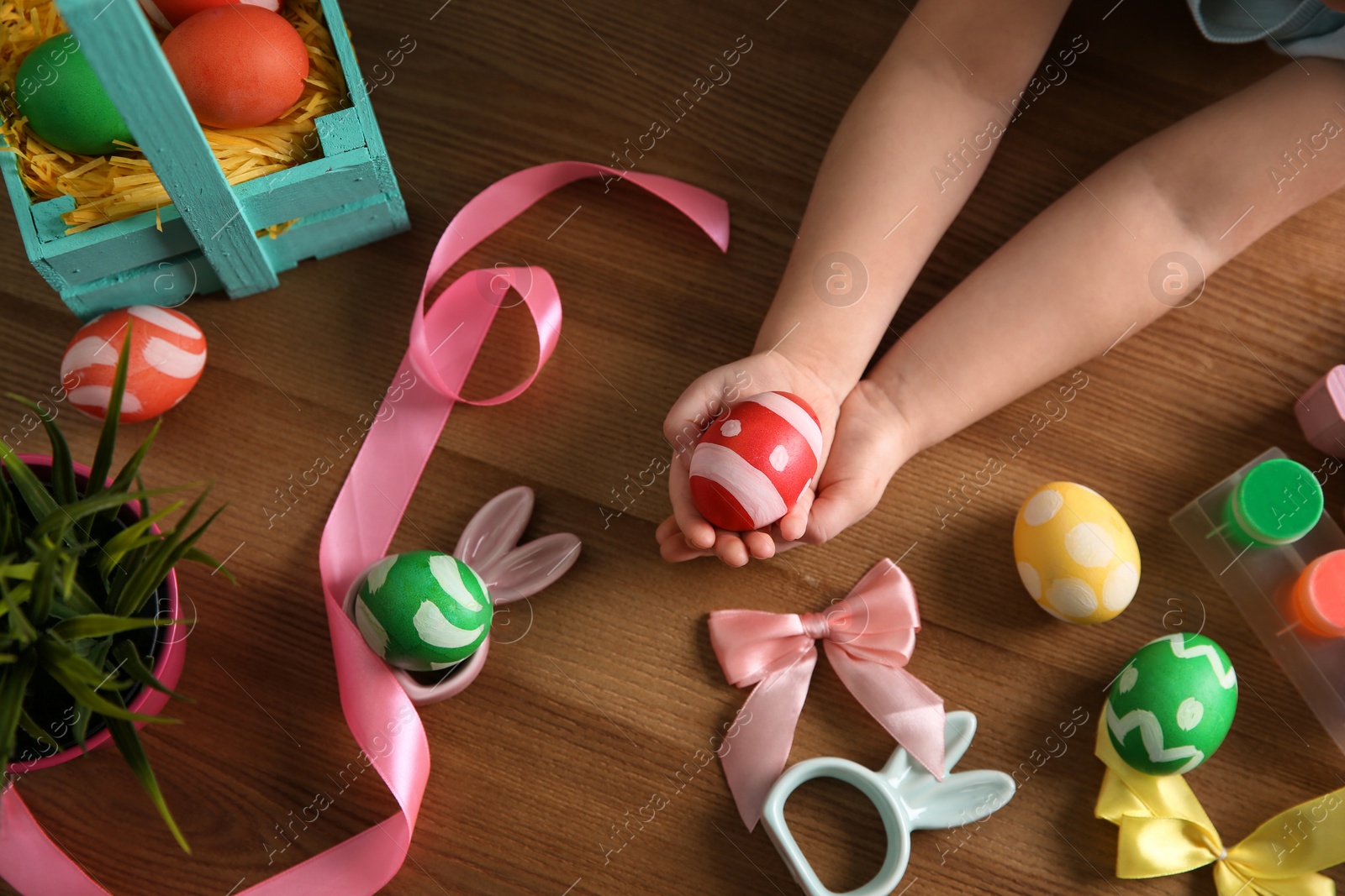 Photo of Little child holding painted Easter egg on wooden background, top view