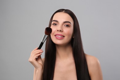 Happy woman applying makeup on light grey background