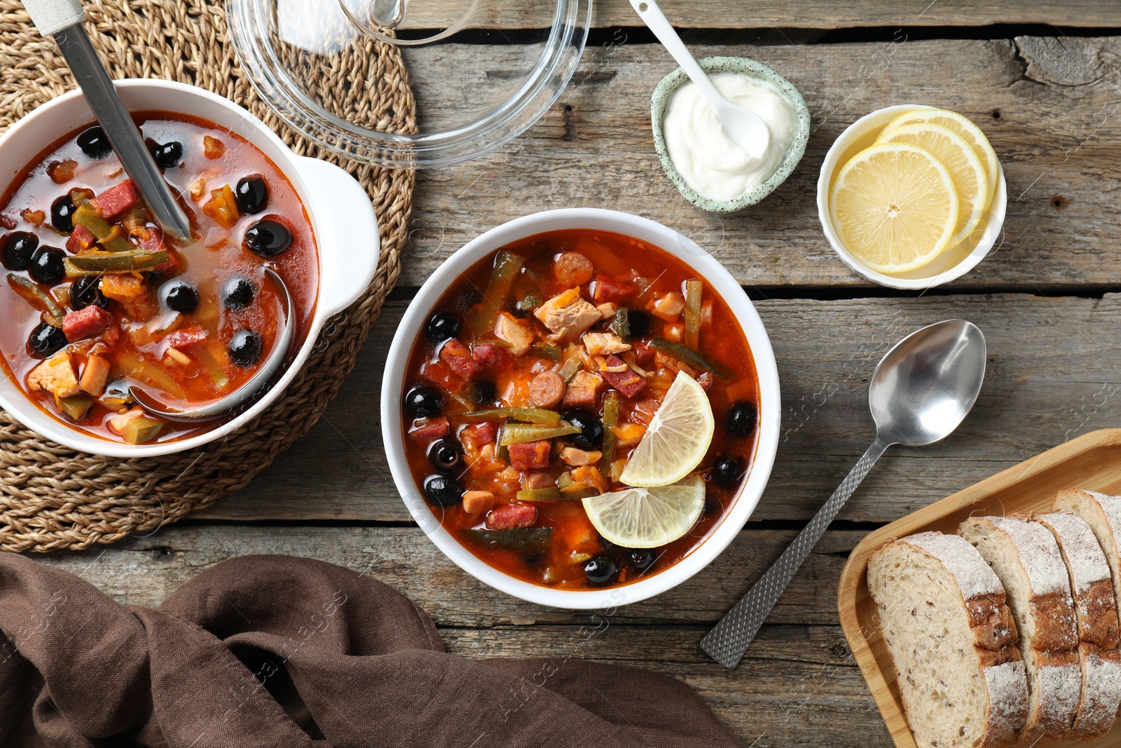 Photo of Meat solyanka soup with sausages, olives and vegetables served on wooden table, flat lay