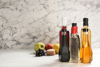 Photo of Bottles with different kinds of vinegar on table against marble background. Space for text