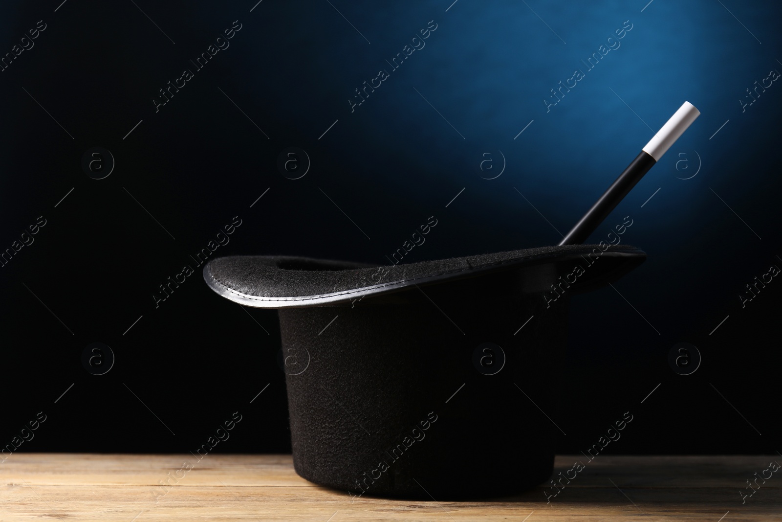 Photo of Magician's hat and wand on wooden table against dark background