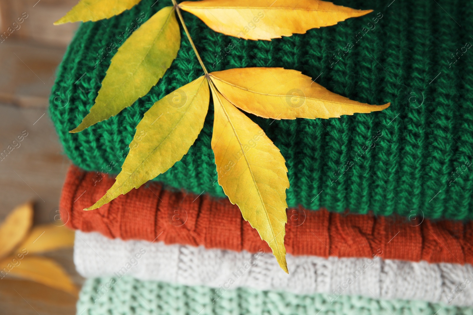 Photo of Stack of warm knitted clothes and autumn leaves on wooden background, closeup