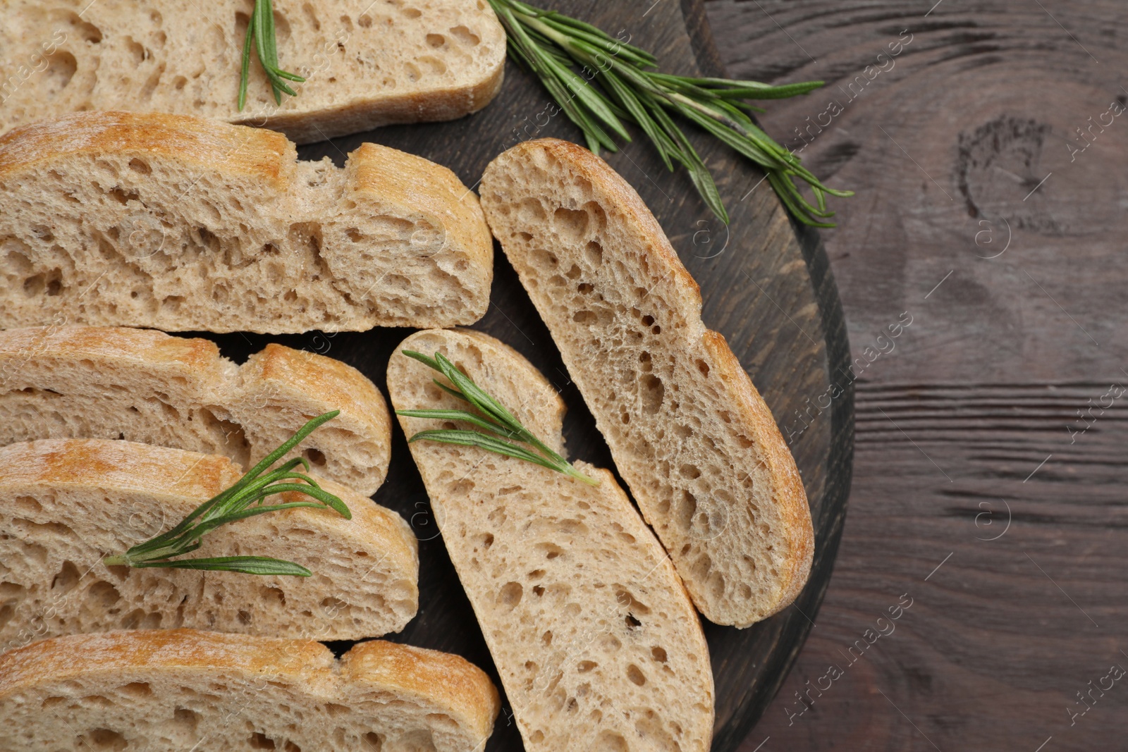 Photo of Delicious ciabatta with rosemary on wooden table, top view