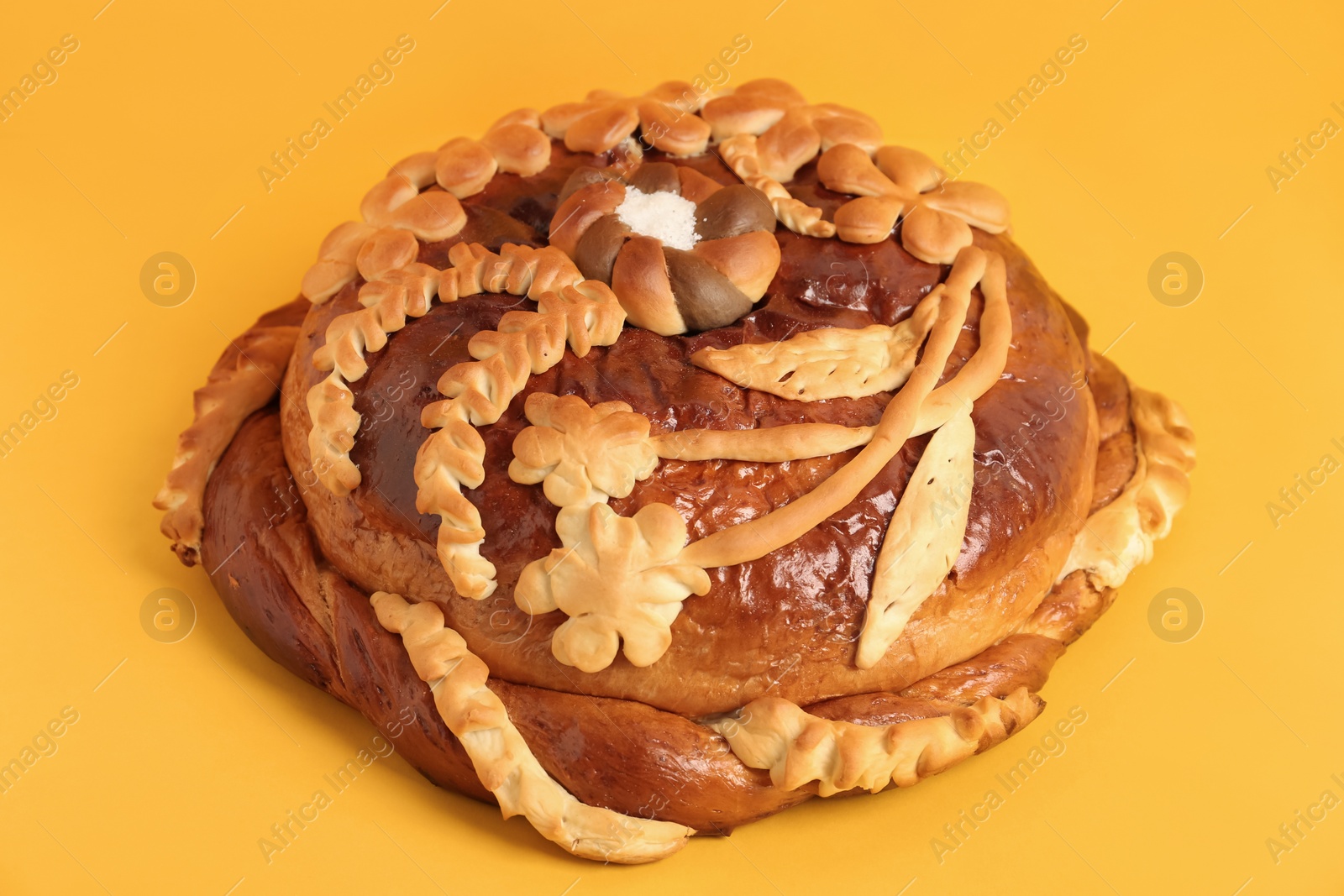 Photo of Fresh korovai on yellow background, closeup. Ukrainian bread and salt welcoming tradition