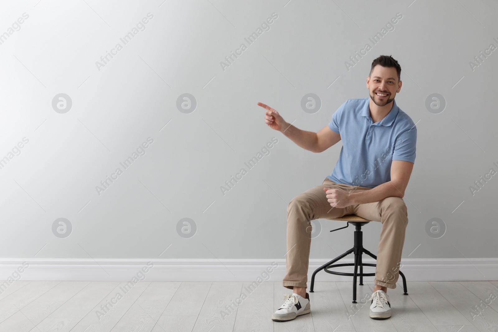 Photo of Handsome man sitting in office chair near grey wall indoors, space for text