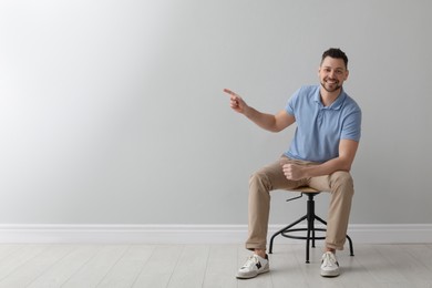 Handsome man sitting in office chair near grey wall indoors, space for text