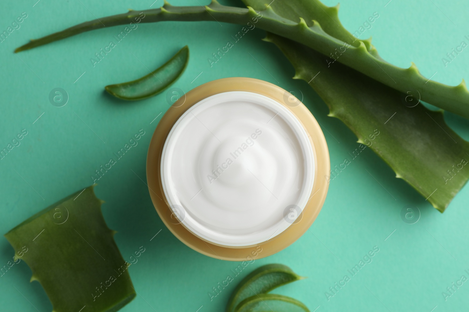 Photo of Jar of natural cream and aloe leaves on green background, flat lay