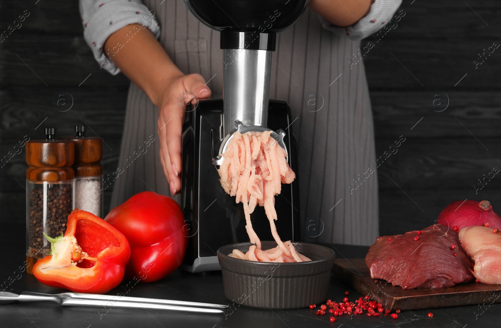 Photo of Woman making chicken mince with electric meat grinder at black table, closeup