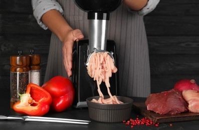 Photo of Woman making chicken mince with electric meat grinder at black table, closeup