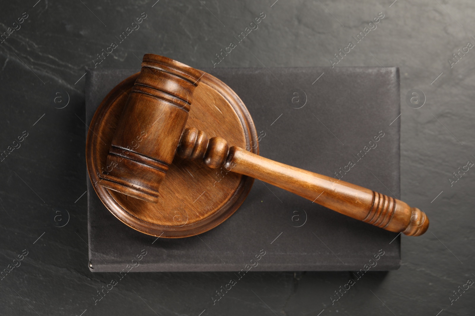 Photo of Wooden gavel, sound block and book on dark textured table, top view