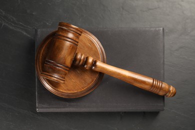 Photo of Wooden gavel, sound block and book on dark textured table, top view