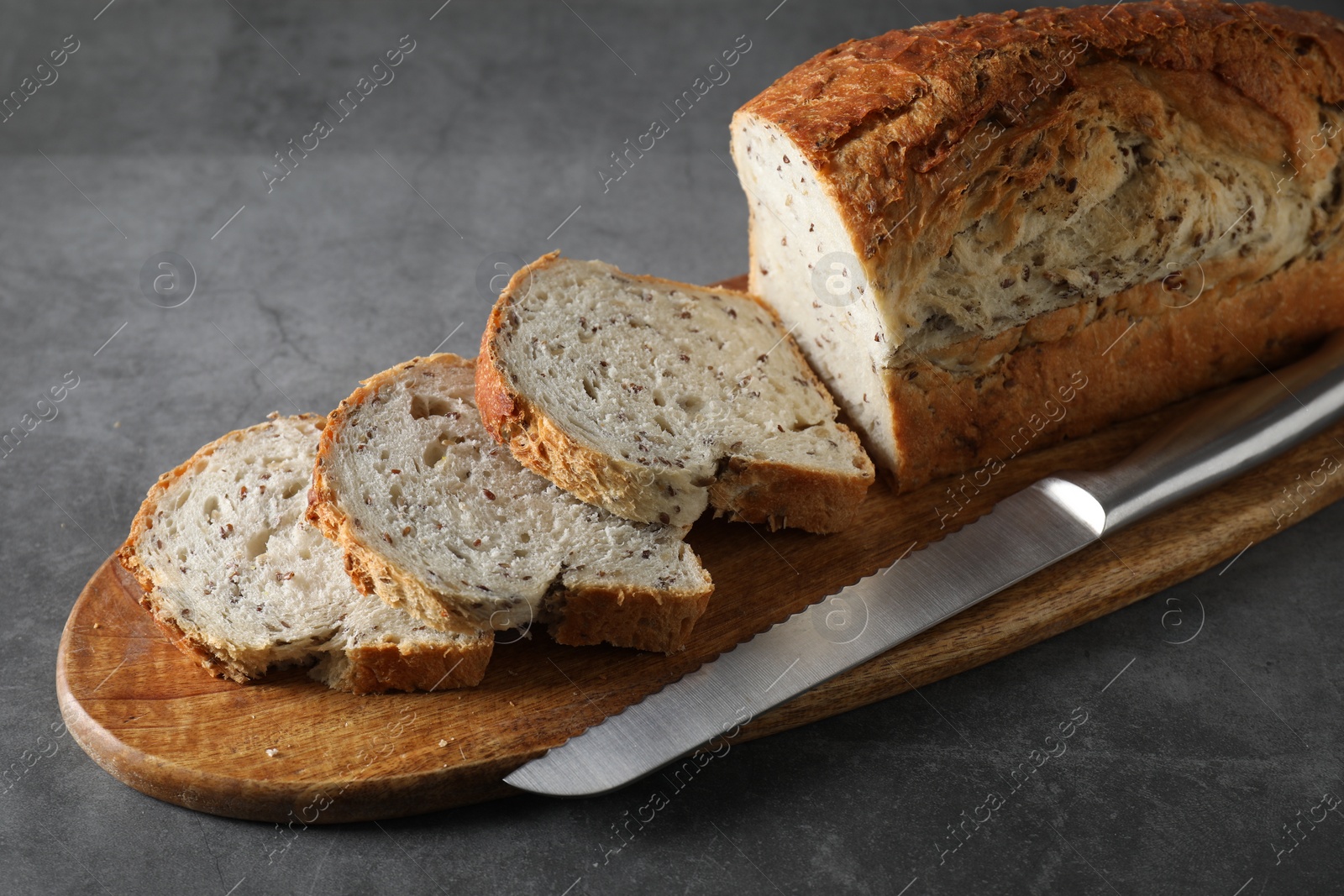 Photo of Freshly baked cut sourdough bread and knife on grey table, closeup