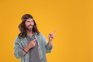 Stylish hippie man pointing at something on orange background, space for text