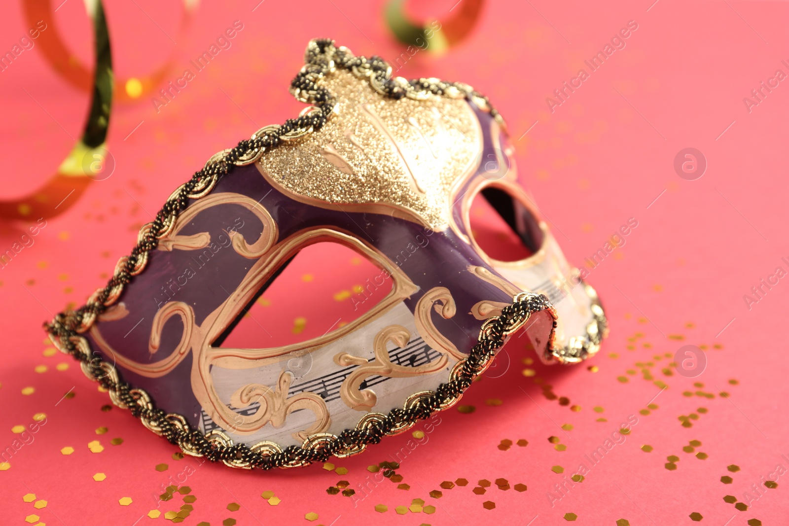 Photo of Beautiful carnival mask with party decor on coral background, closeup